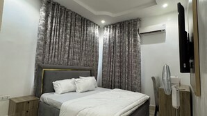 Ein modernes Schlafzimmer mit einem großen Bett, einem Nachttisch, einem an der Wand montierten Fernseher und einem Deckenventilator.