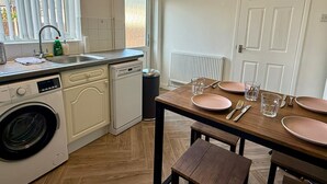 Uma cozinha compacta com máquina de lavar, lava-louças e área de refeições com mesa posta para dois.