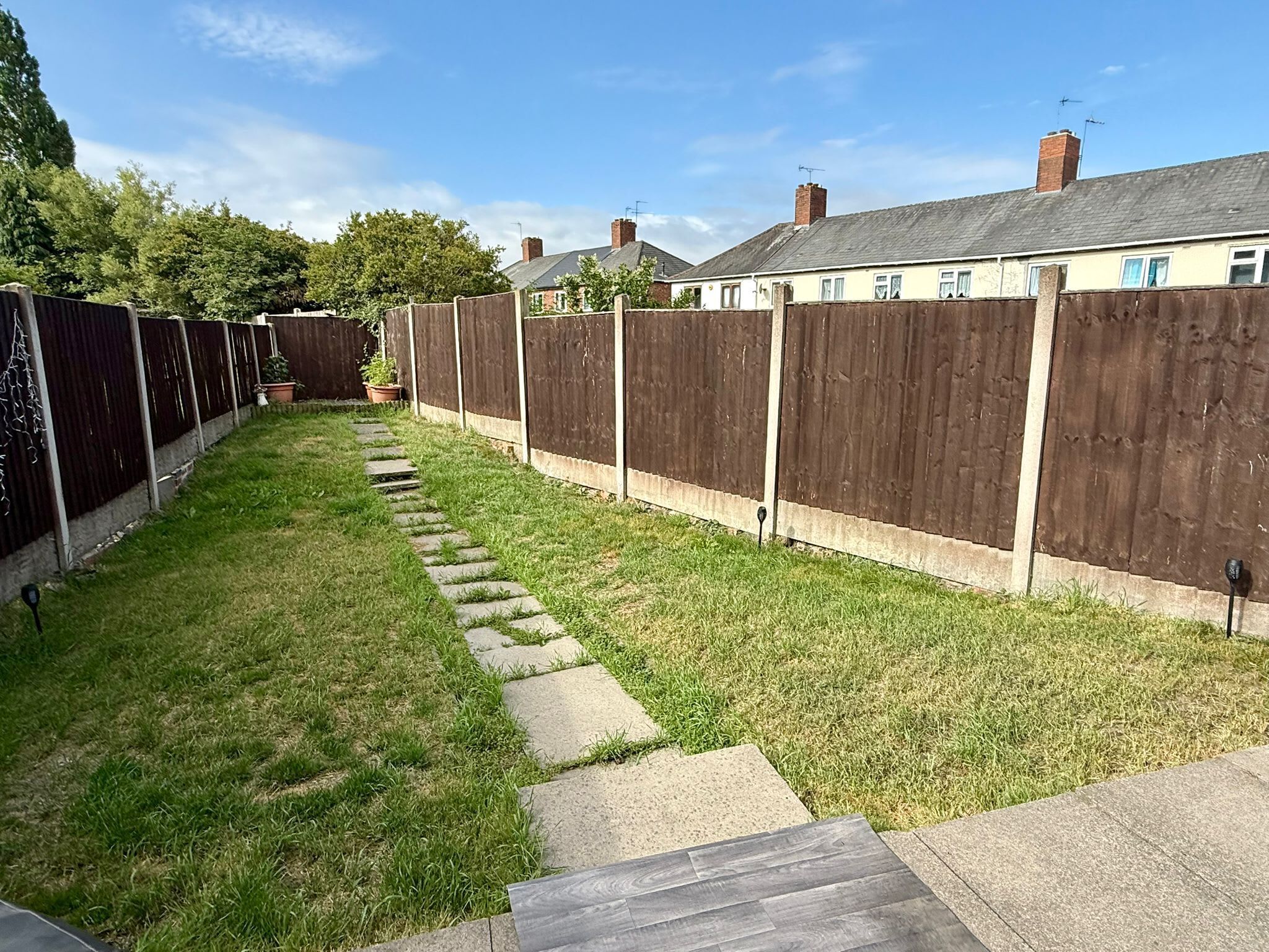 A narrow backyard with a wooden fence, a stone pathway, and a grassy area.
