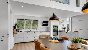 Une cuisine moderne avec des meubles blancs, un grand îlot central et un coin repas comprenant une table et des chaises en bois.