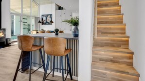 Une cuisine moderne dotée d’un îlot central, de tabourets de bar et d’un escalier avec des marches en bois et un éclairage intégré sous les marches.