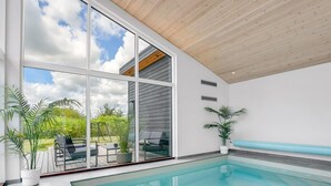 Une piscine intérieure moderne avec un mur en verre, un plafond en bois et une vue sur la verdure environnante.