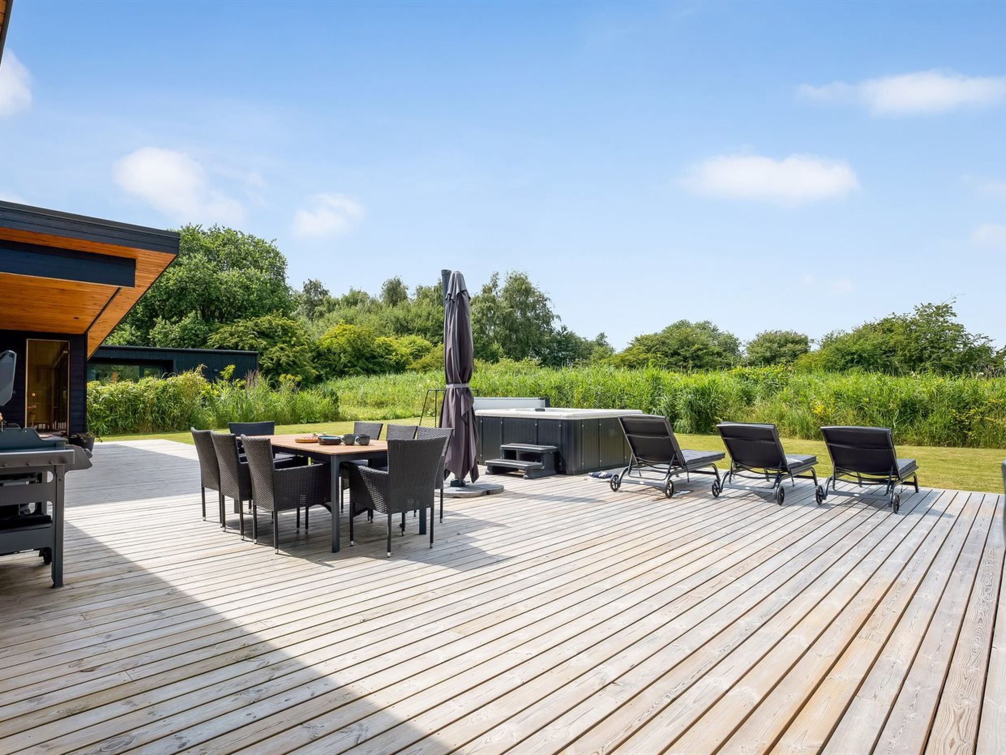A wooden deck with outdoor furniture, including a table and chairs, and a hot tub.