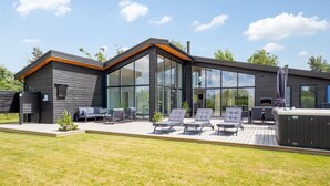 Une maison moderne dotée d’un patio aménagé avec des chaises longues et un jacuzzi.