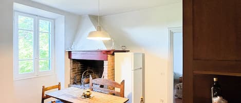 A dining area with a wooden table and chairs, a hanging light fixture, and a brick fireplace.