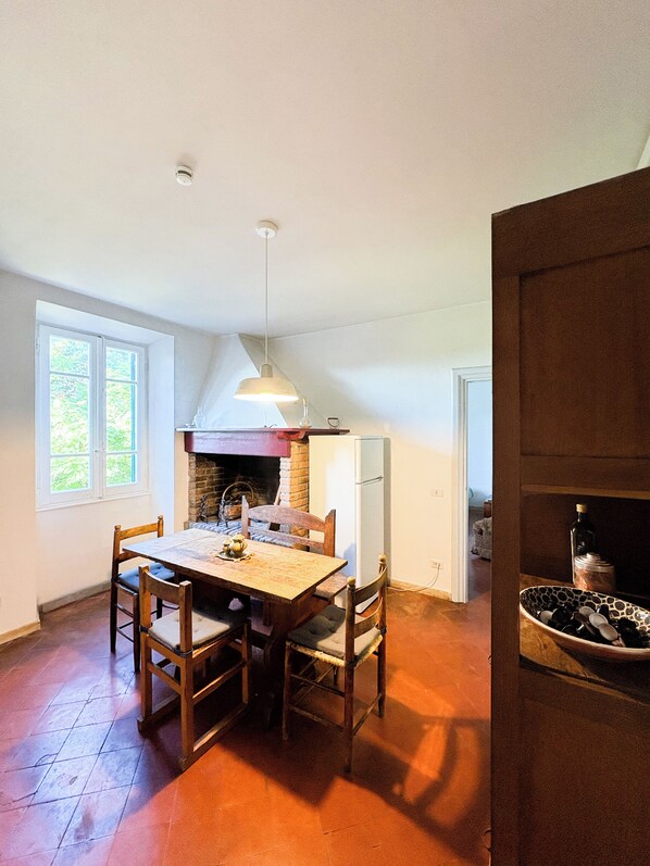 A dining area with a wooden table and chairs, a hanging light fixture, and a brick fireplace.