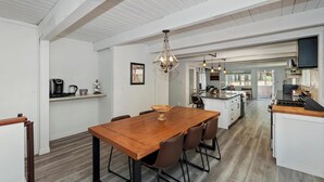 Una cocina amplia con una isla central, armarios blancos y un comedor con mesa y sillas de madera.