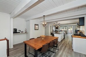 Una cocina amplia con una isla central, armarios blancos y un comedor con mesa y sillas de madera.