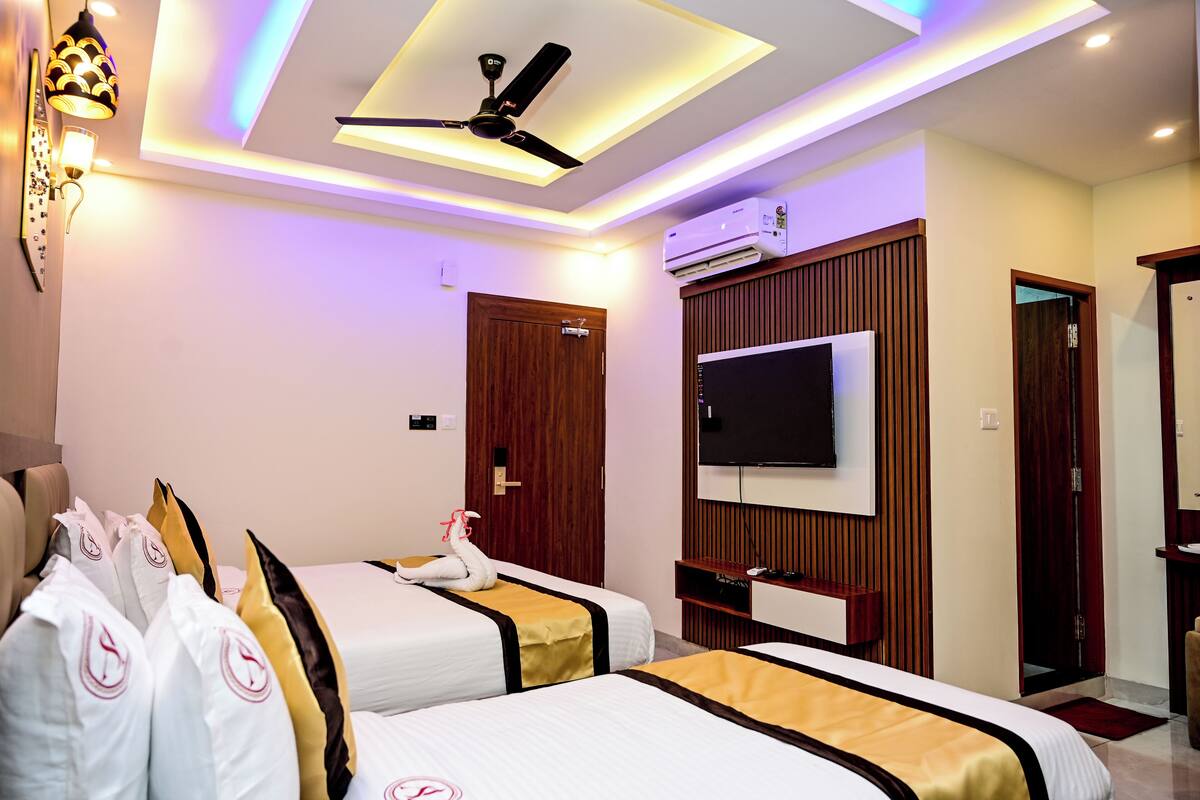 A hotel room with two beds, a ceiling fan, a flat-screen TV, and an air conditioning unit.