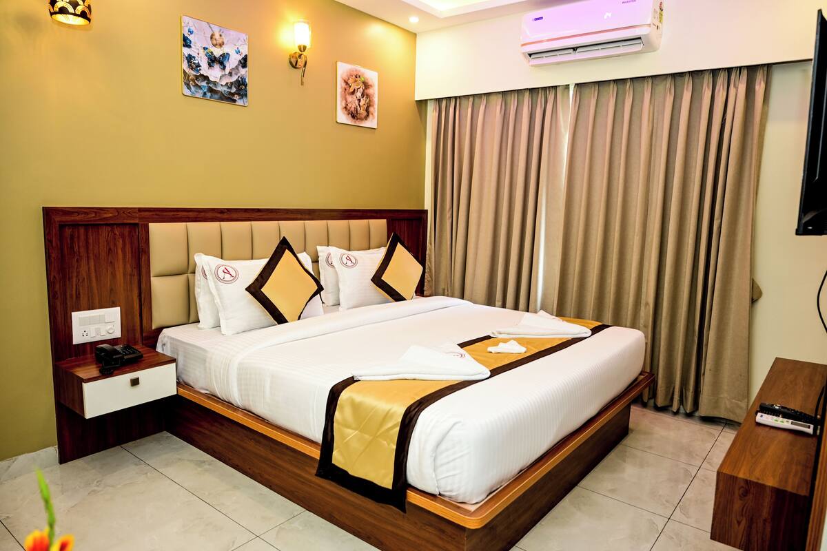 A hotel room with a large bed, a bedside table with a phone, a flat-screen TV, and a window with curtains.