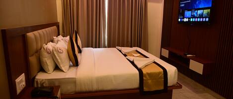 A hotel room with a bed, a TV mounted on the wall, and a window with curtains.