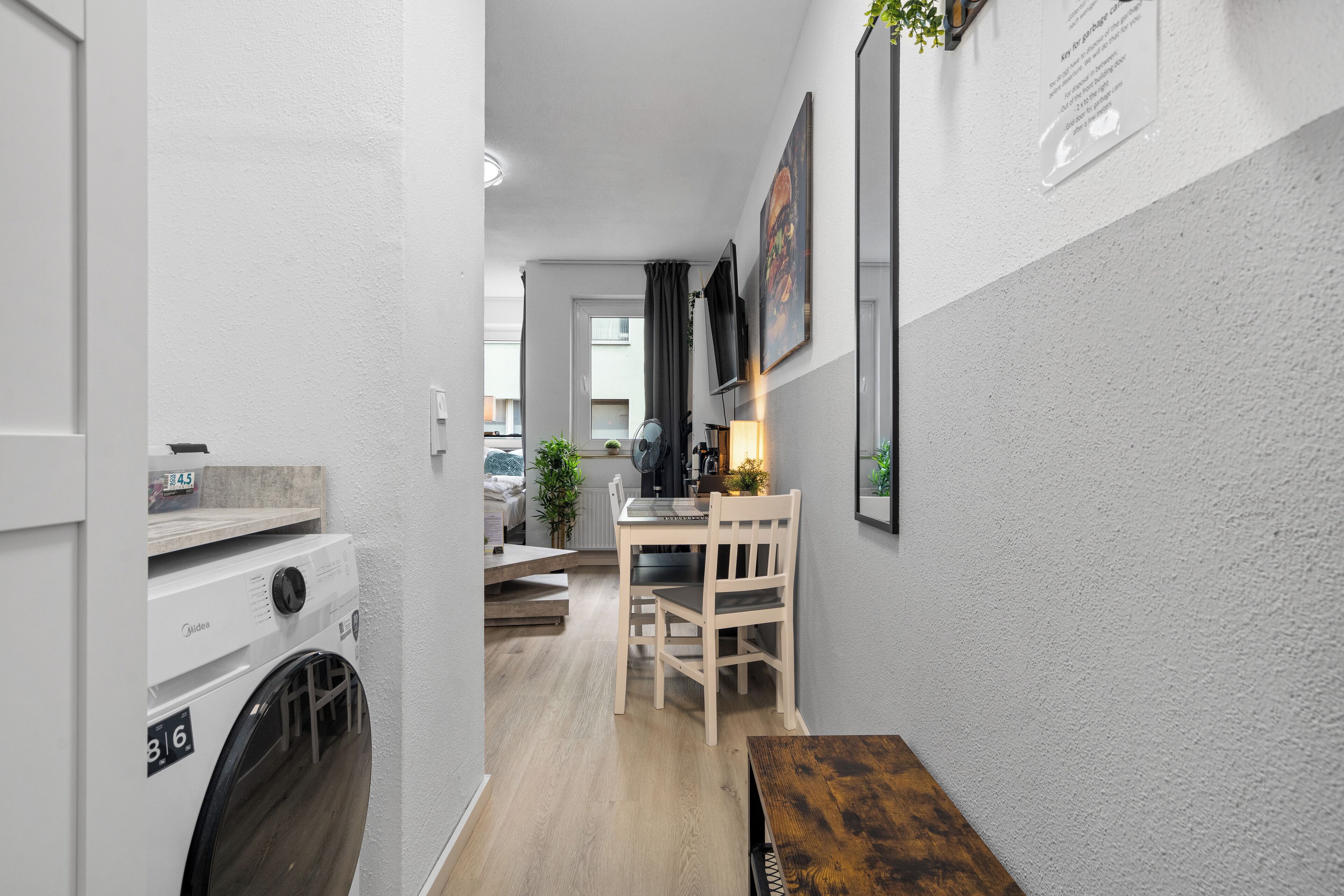 A laundry room with a washing machine, a drying rack, and a wooden bench.