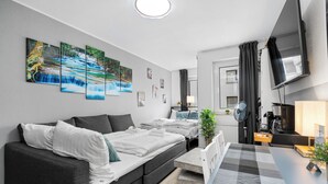 A modern hotel room with a sofa bed, a dining table, a TV, and a painting of a waterfall on the wall.