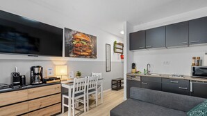 A modern kitchen with a dining area, grey sofa, and a large flat-screen TV.