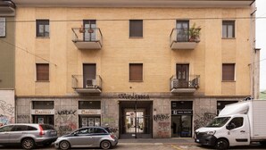 A multi-story building with a beige facade, featuring balconies, storefronts including a nail salon, and graffiti on the walls. - Cosy two-room apartment Porta Romana - Mirable PM (Milan)