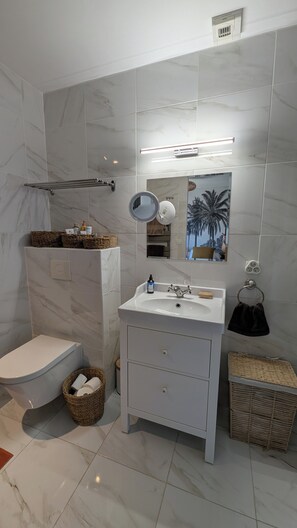 A modern bathroom with a toilet, sink, and shower. There are wicker baskets and a towel rack. - Beautiful villa with a pool, in a quiet location near Avignon   (Roquemaure)