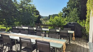 Un espace extérieur aménagé pour les repas, avec une longue table et des chaises, un barbecue et une pergola.