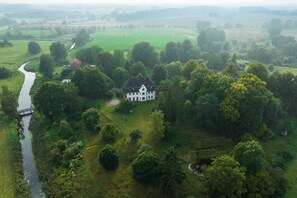 Ein großes, weißes Haus mit schwarzem Dach, umgeben von üppigem Grün und einem Fluss.