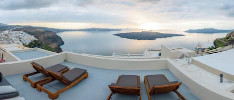 Una terraza en la azotea con tumbonas de madera y vistas a un mar tranquilo y a islas lejanas.