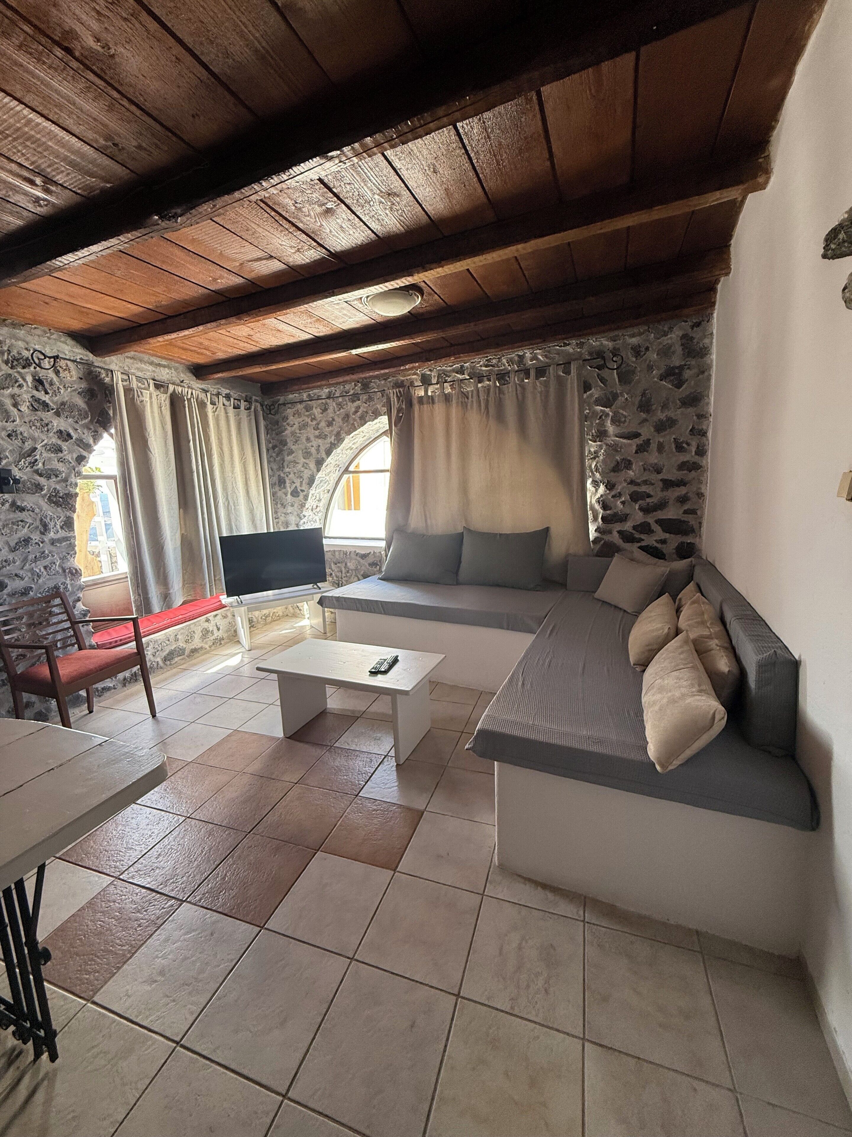 Una sala de estar acogedora con pared de piedra, techo de madera, un sofá, televisor y una mesa de centro.