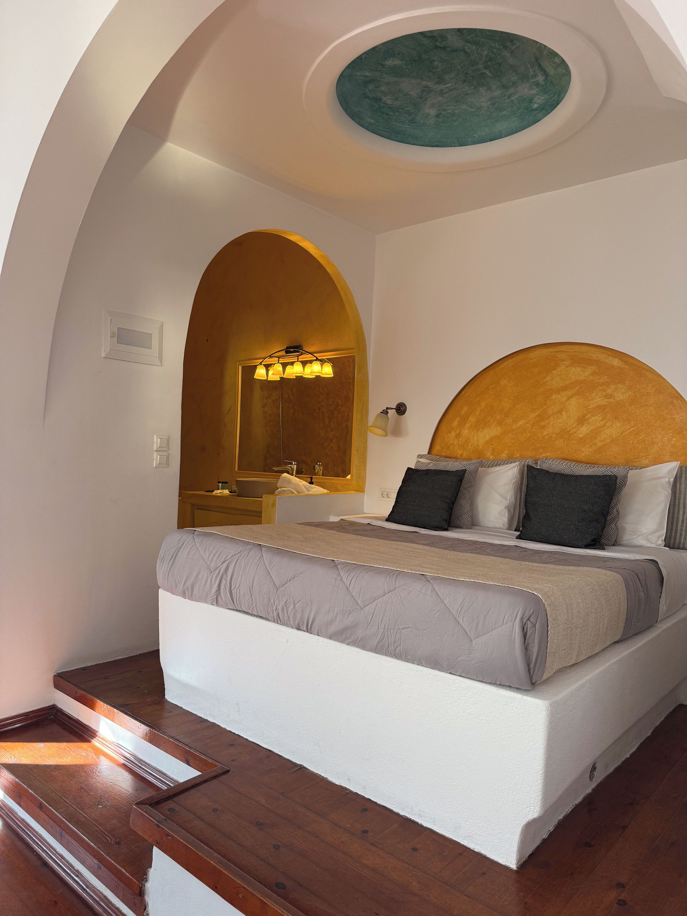 A bedroom with a bed, wooden floor, a circular skylight, and a mirror above the bed.