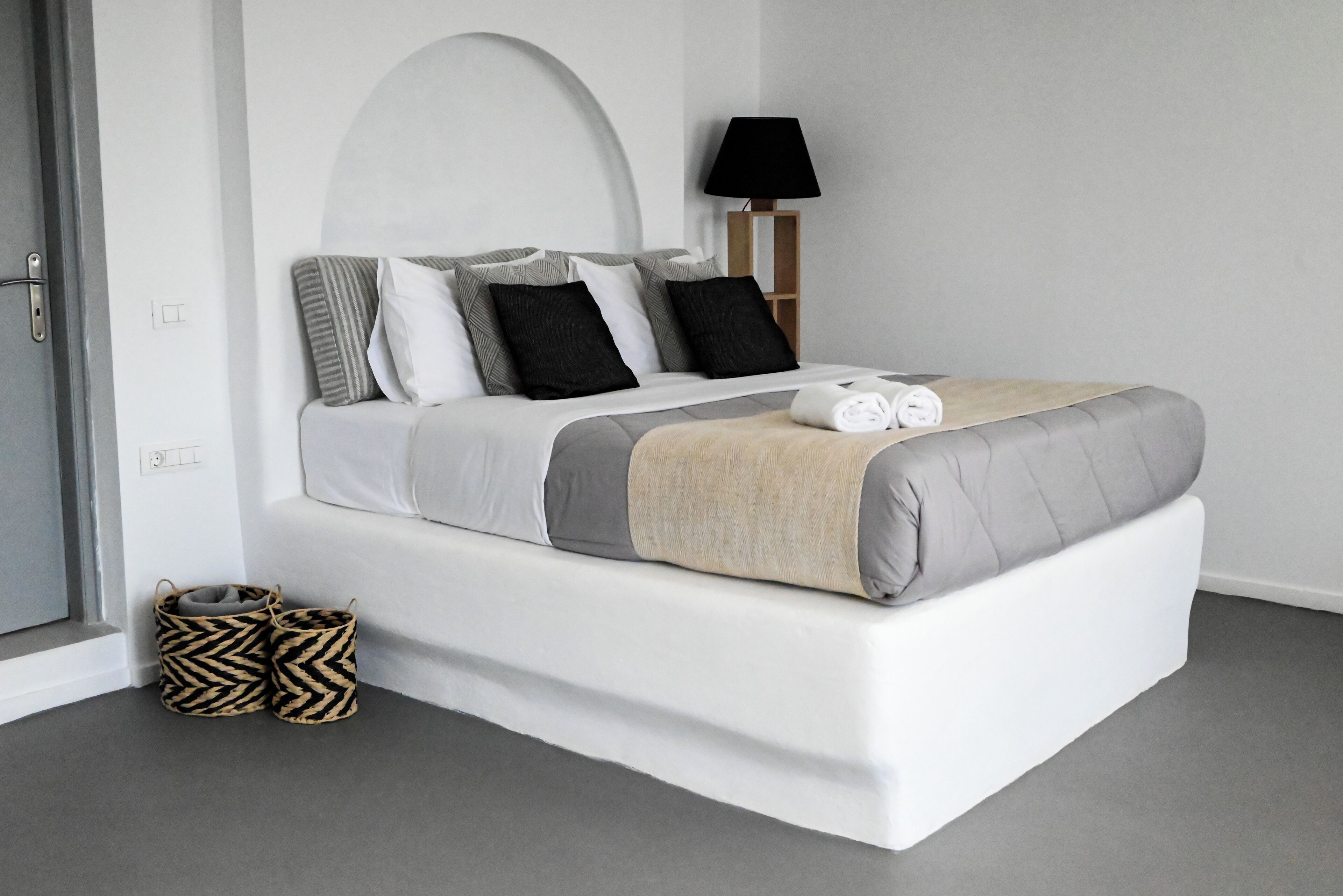 A modern bedroom with a large bed, a bedside lamp, and storage baskets.