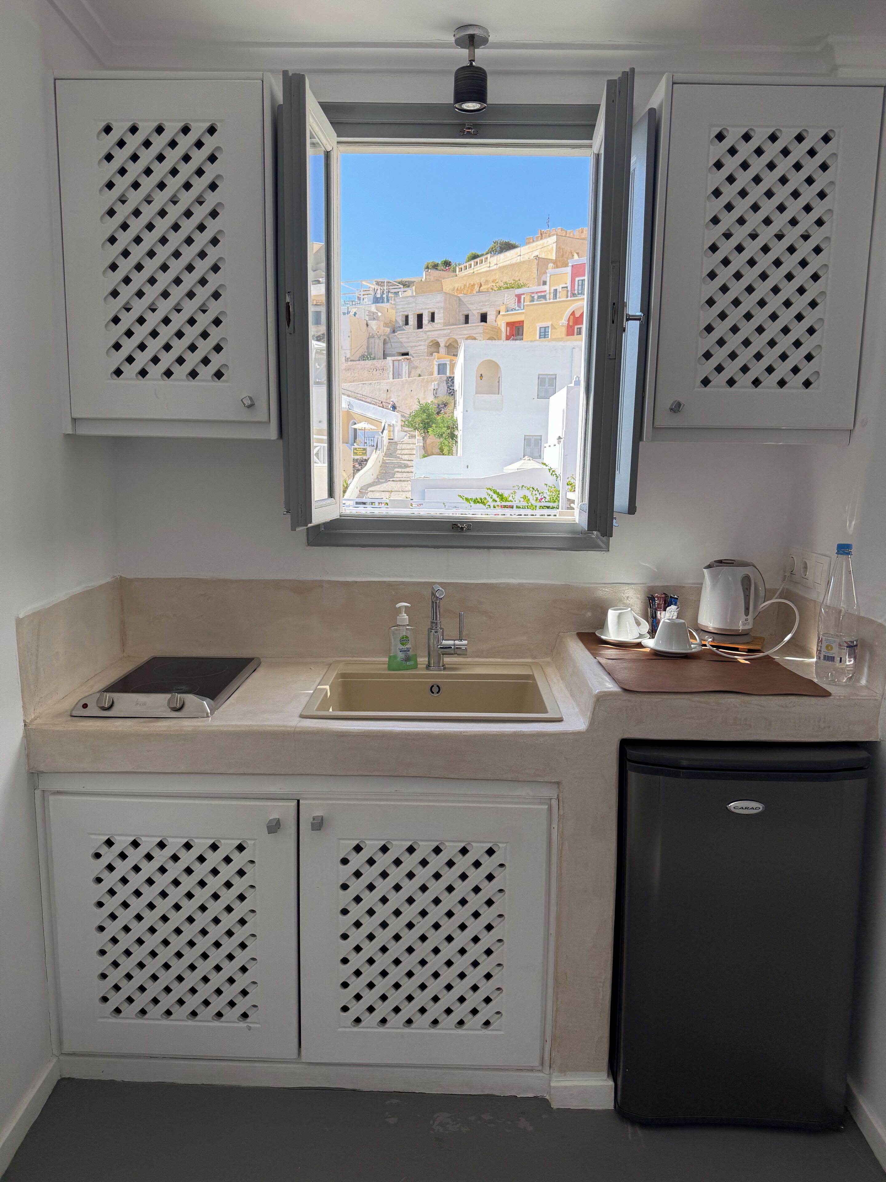 A compact kitchen with a window view of a cityscape, a sink, a stove, and a refrigerator.