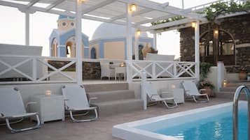 Un espace extérieur avec une piscine, des chaises longues, une pergola et un bâtiment en pierre surmonté d’un dôme, visible au fond.