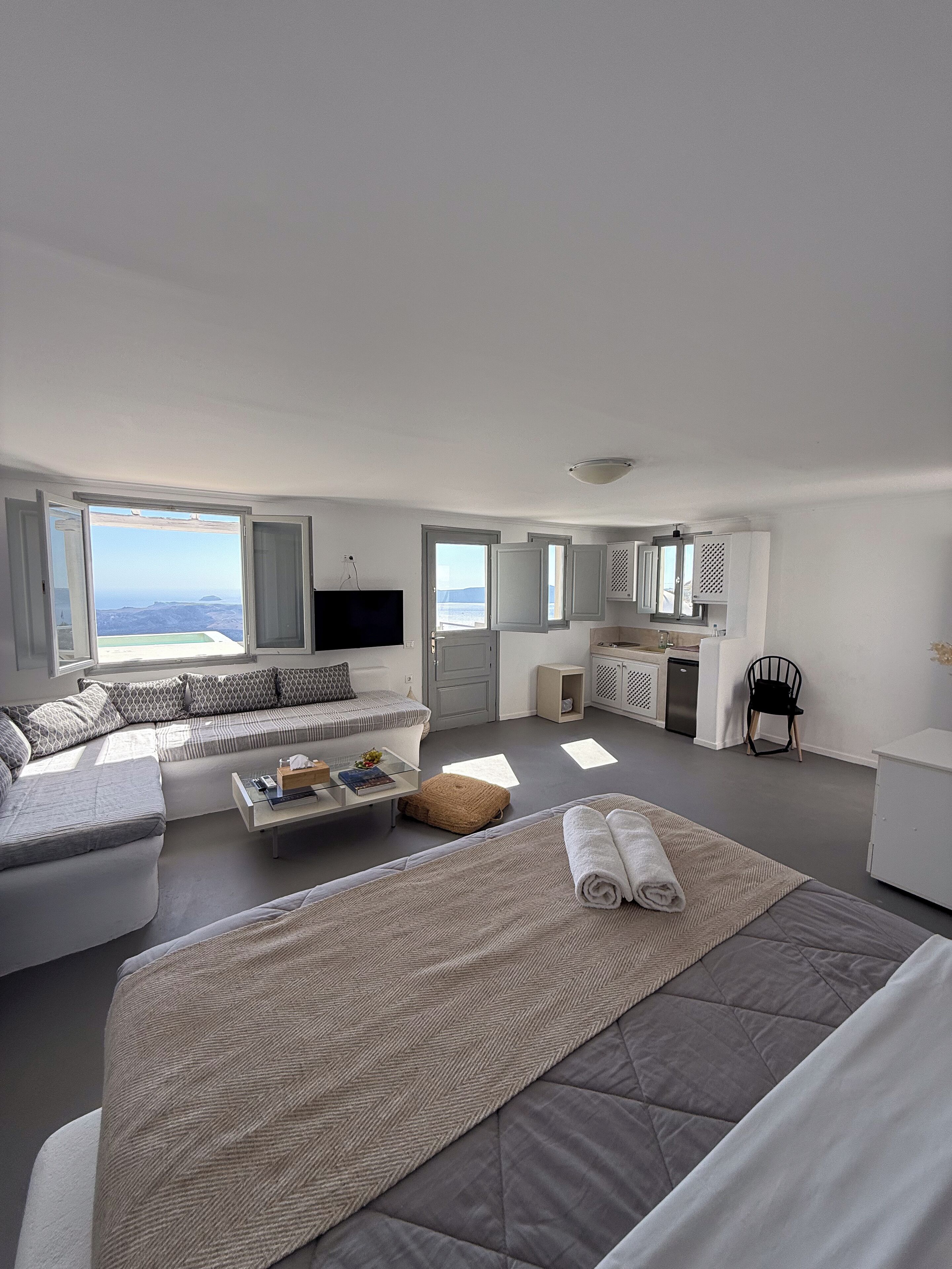 Habitació moderna i ben il·luminada amb un llit gran, un sofà, una taula de cafè petita i vista al mar a través de grans finestres.