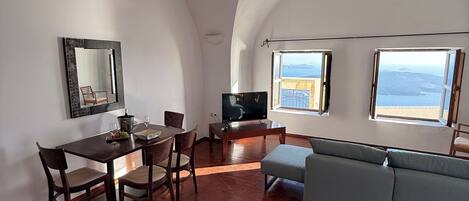 Amplia sala de estar con mesa de comedor, sillas, sofá, televisor y ventanas grandes con vista al mar.