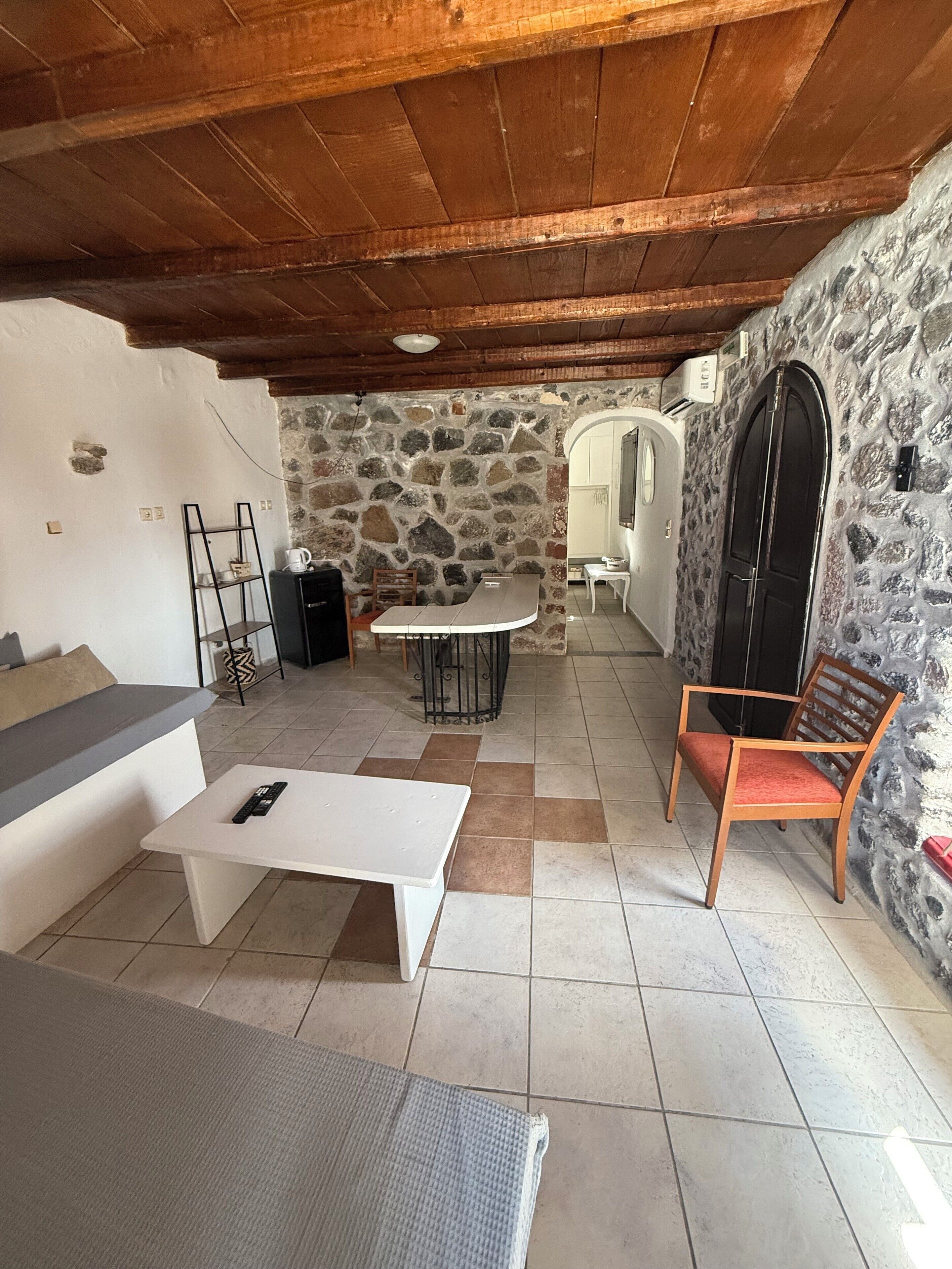 Um quarto aconchegante com parede de pedra, teto de madeira, sofá branco, mesa pequena e uma cadeira.