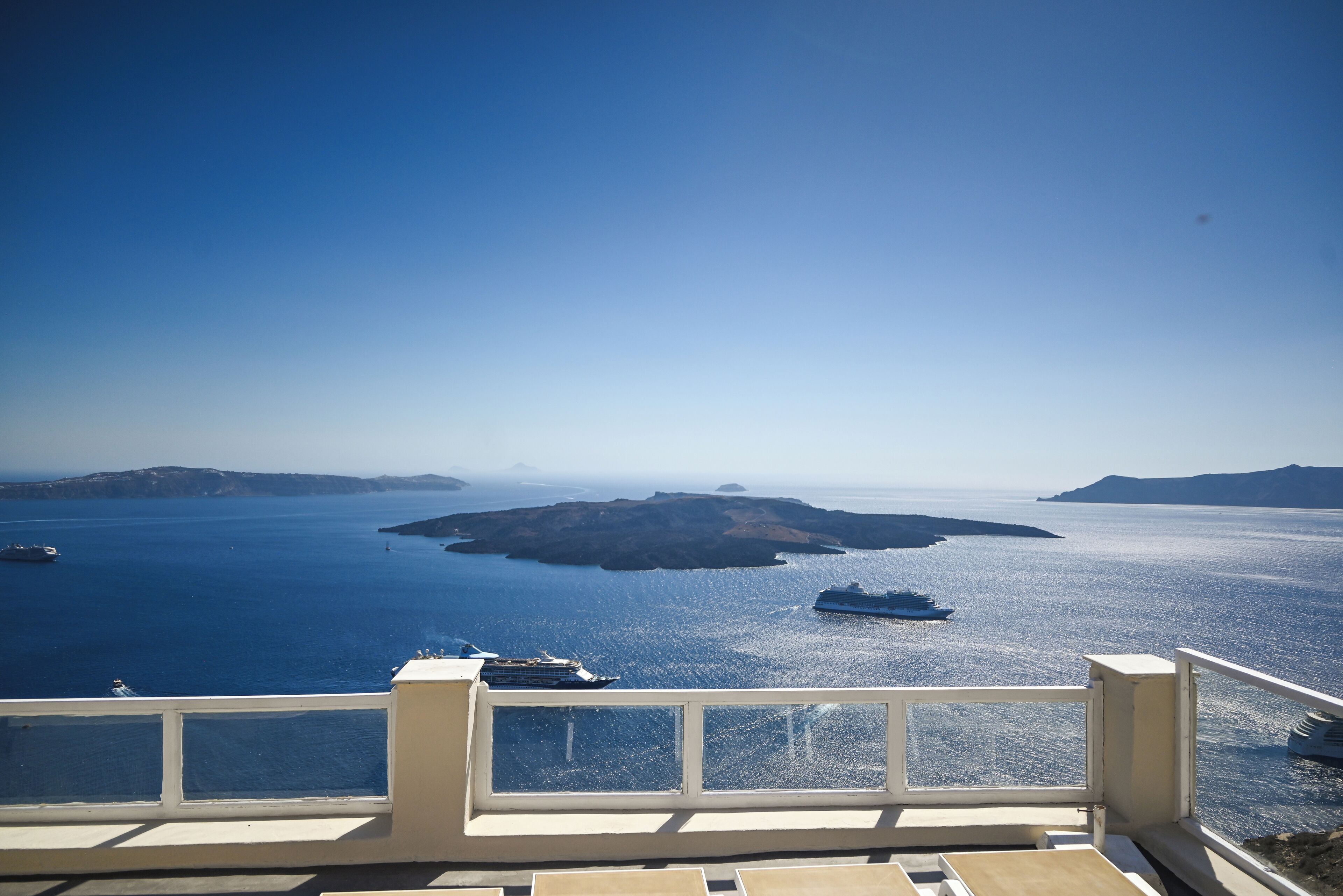 Une vue depuis un balcon donnant sur une vaste étendue d’eau, avec des bateaux, un ciel dégagé et des reliefs lointains.