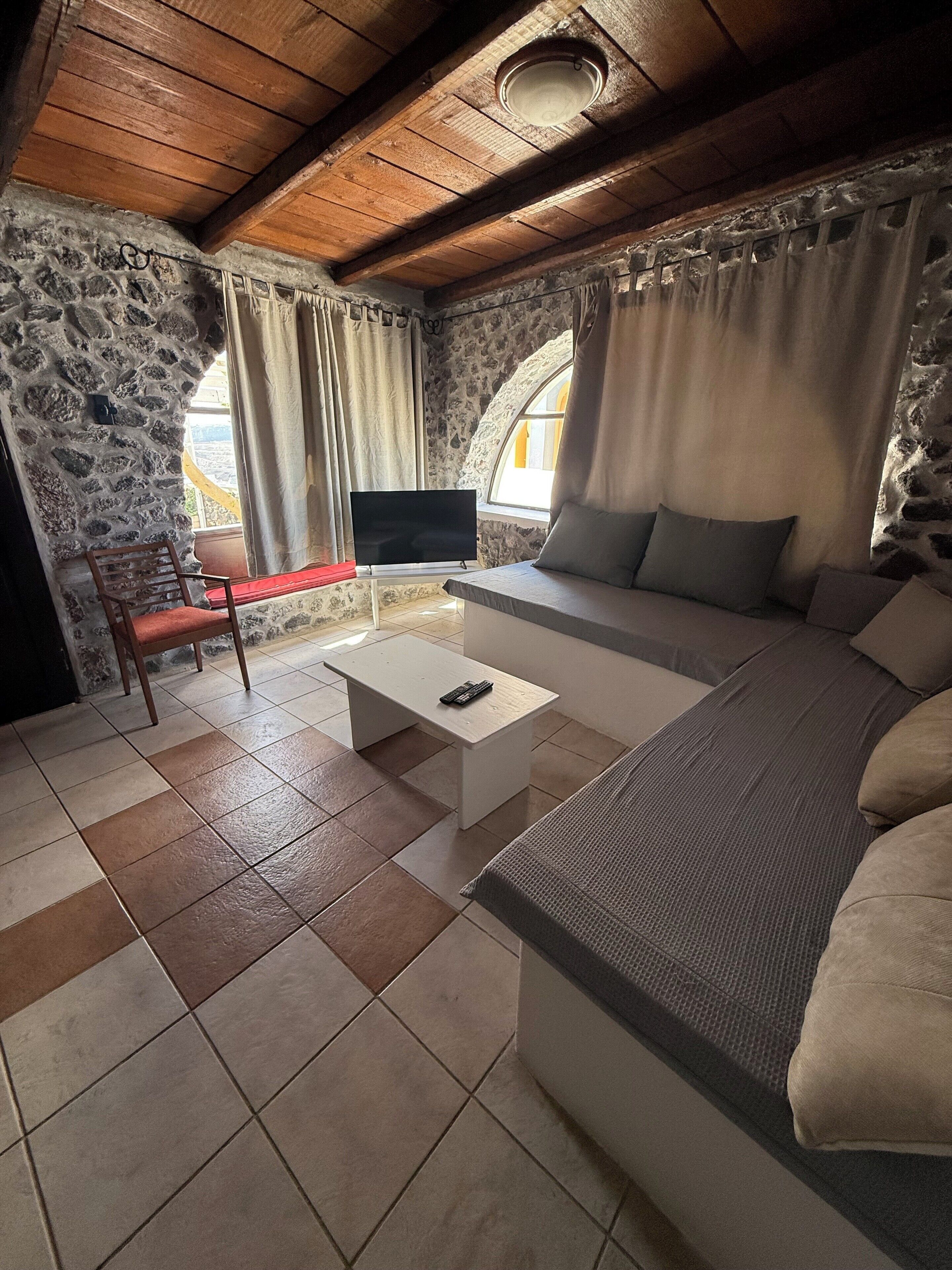 A cozy room with a stone wall, wooden ceiling, a sofa, a TV, and a chair.