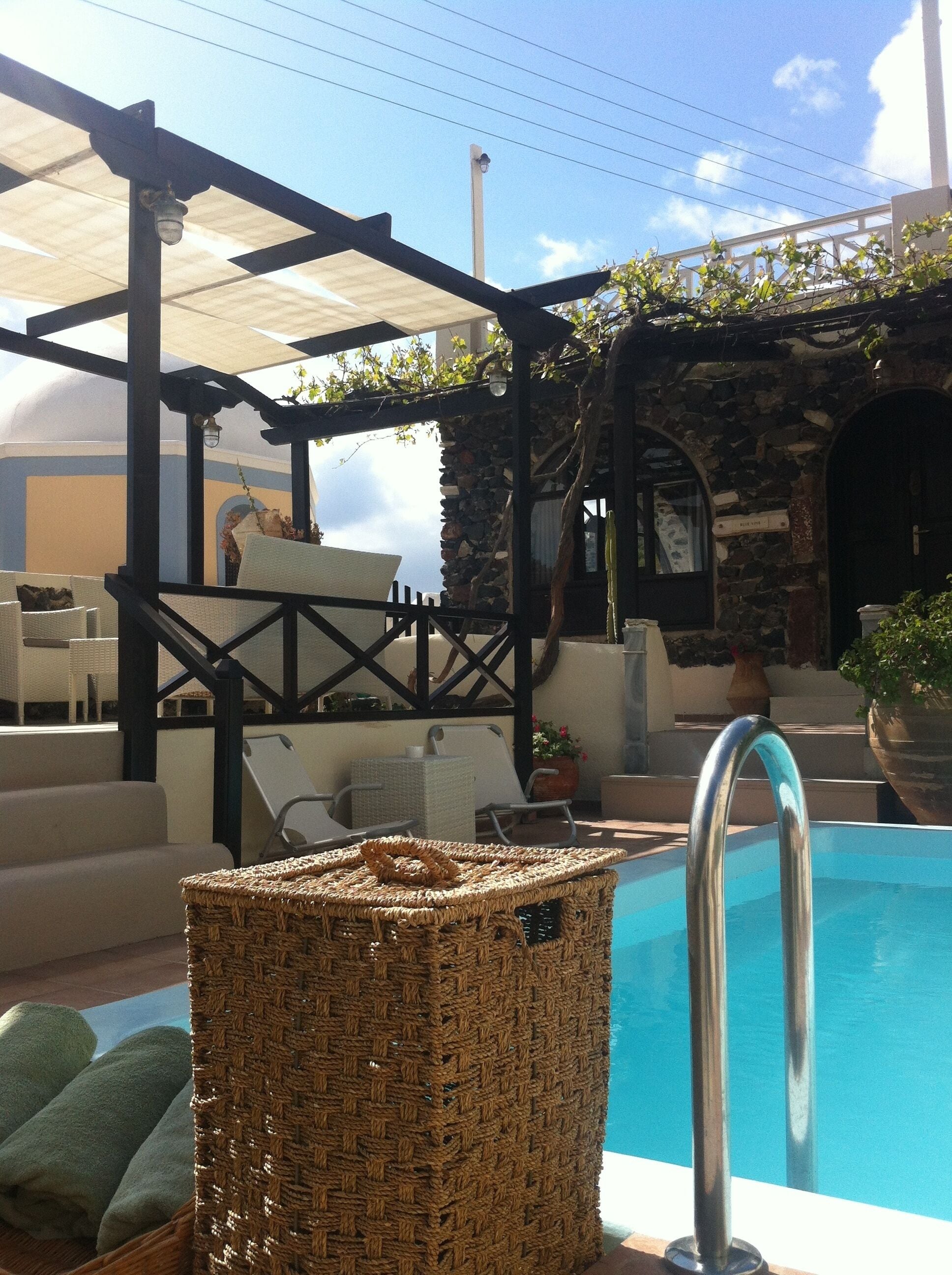 Un área de piscina con pérgola, sillas de descanso y una pared de piedra.