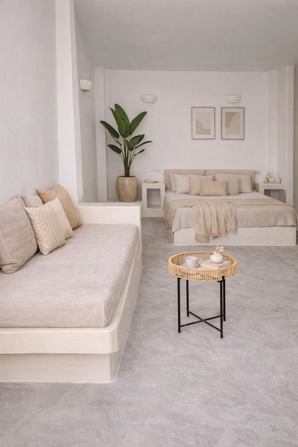 A minimalist bedroom with a large bed, a smaller sofa, a bedside table with a basket, and a potted plant.