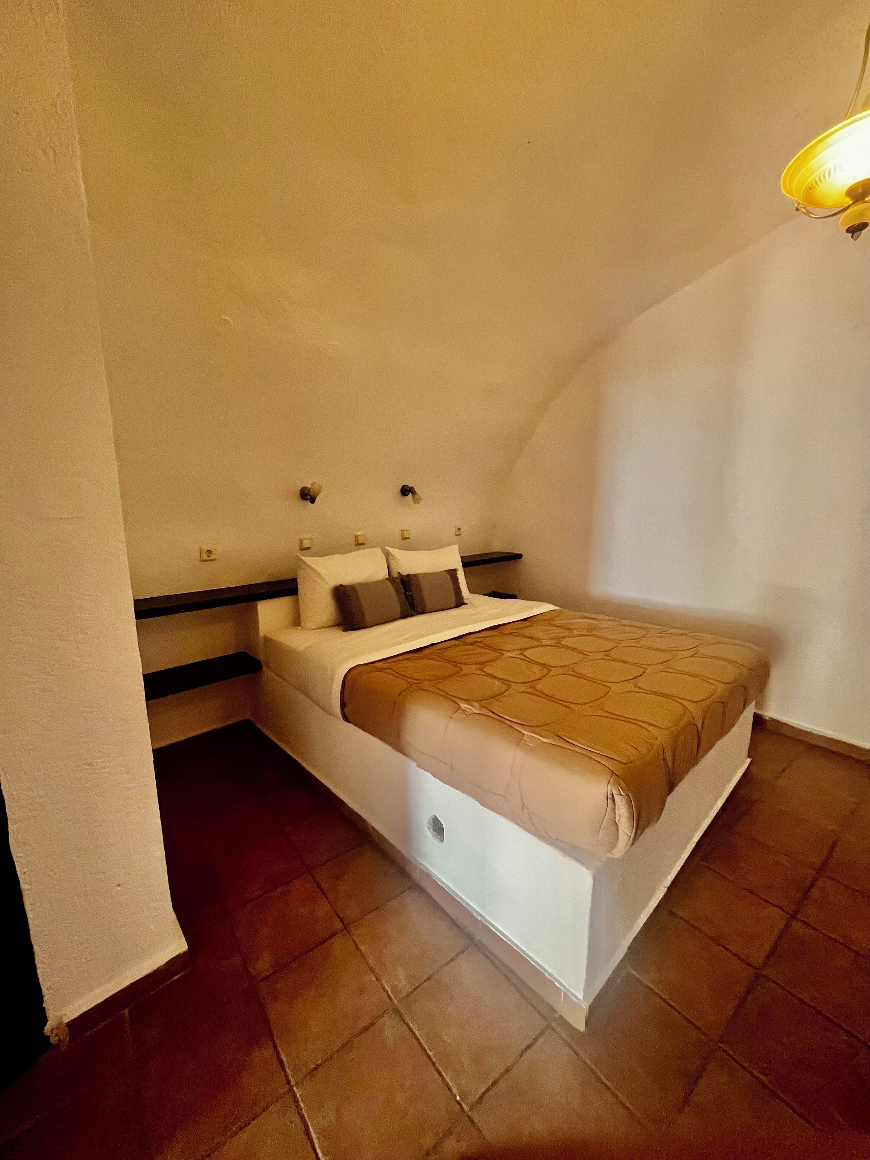 A bedroom with a bed, a nightstand, a wall-mounted lamp, and a ceiling light.