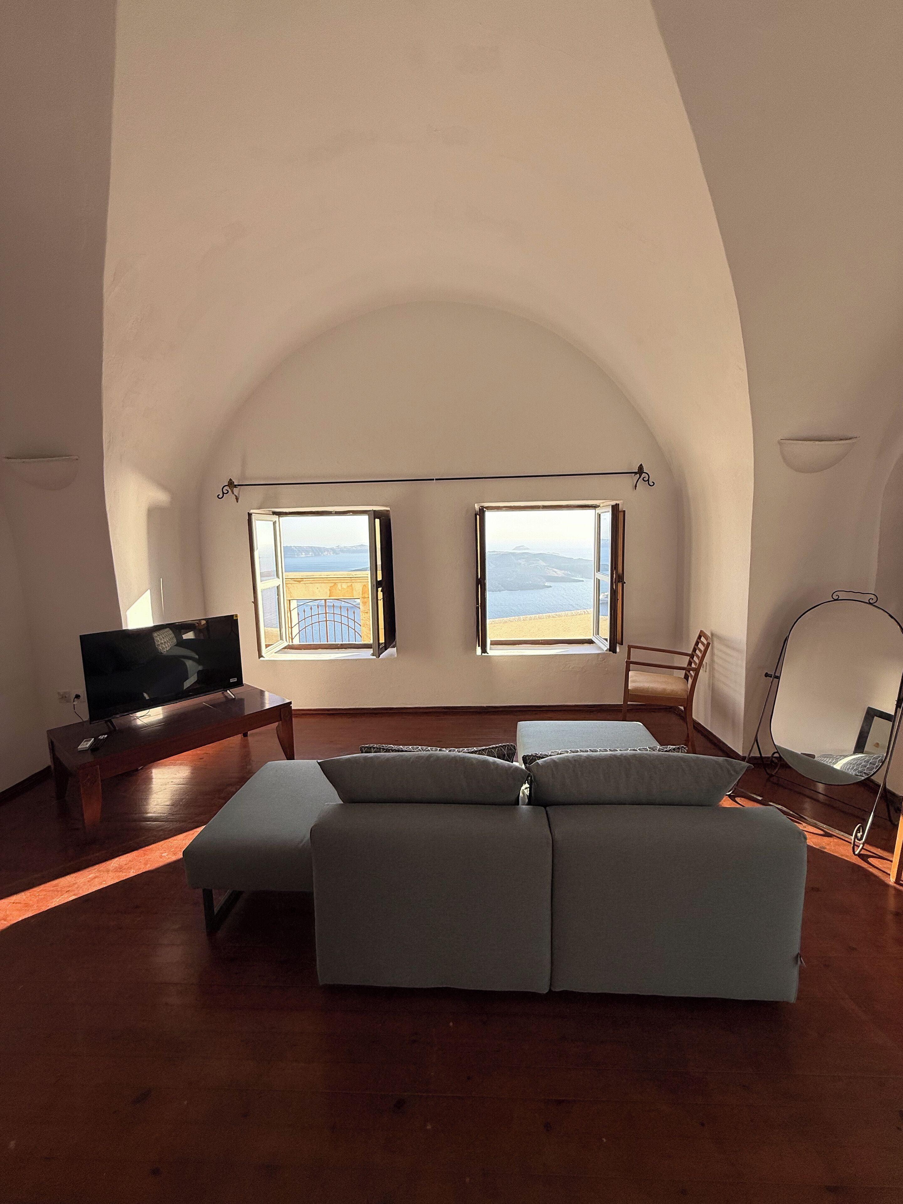 Un salon spacieux avec un grand canapé, un téléviseur et deux fenêtres donnant sur la mer.