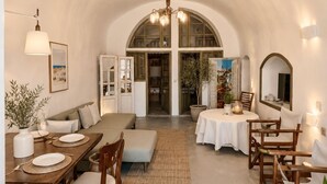 Uma sala de jantar com teto alto e arqueado, uma mesa redonda, cadeiras de madeira e um lustre central.