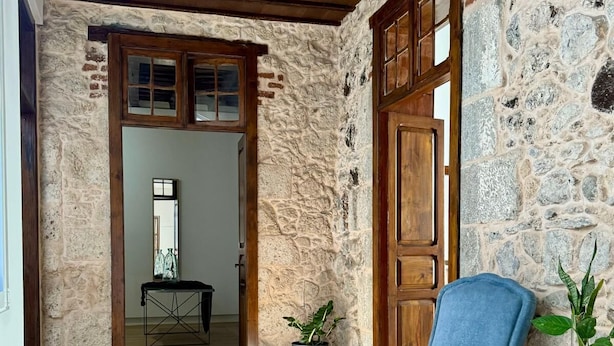 A room with a wooden floor, a blue armchair, a wooden door, and a stone wall. - Doña Perfecta -El 11 De López Botas-. (Las Palmas)