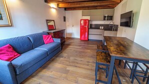 Um espaço compacto com sofá, frigorífico vermelho, mesa de jantar de madeira e zona de cozinha.