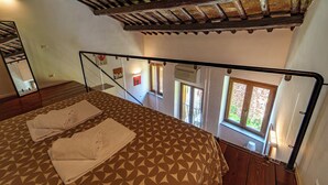 Quarto com colcha estampada, um espelho e vista exterior pela janela.