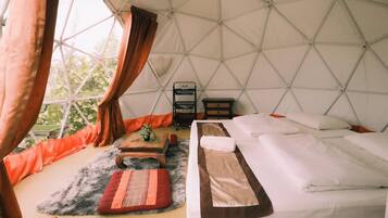 A cozy, well-lit tent with a bed, a small table, and a chair.