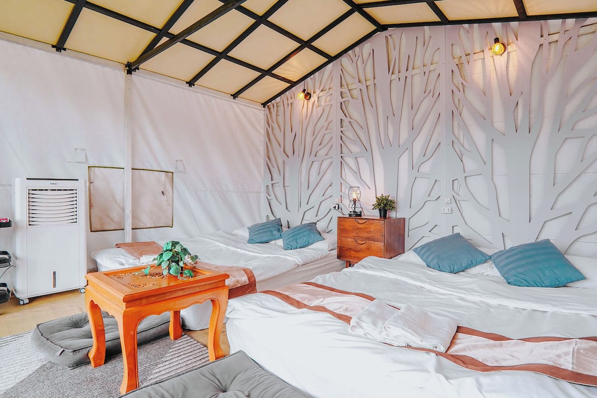 A room with two beds, a wooden table, a white wardrobe, and a wall with a tree design.
