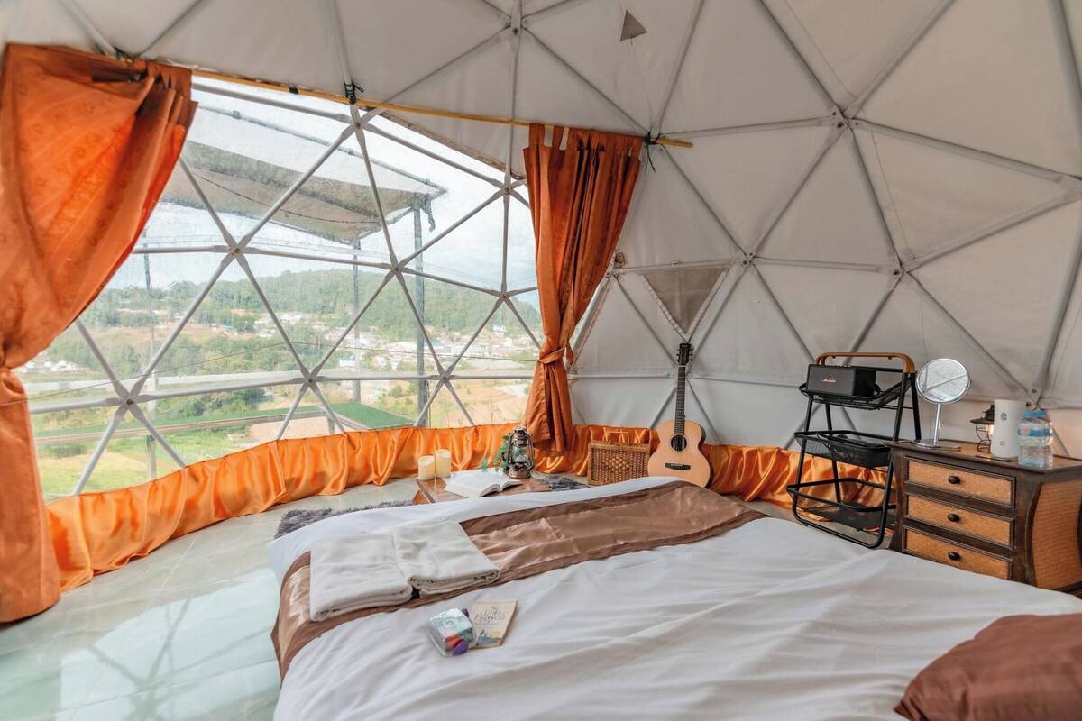 A tent-style room with a bed, curtains, a guitar, and a small table with a mirror and a water bottle.