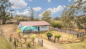 A house with a red roof, surrounded by a fenced yard with sparse vegetation and a dirt path leading to the entrance. - Forest View Self Catering (Krugersdorp)
