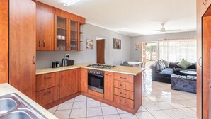 A kitchen with wooden cabinets, a gas stove, and a dining area with a sofa and table. - Forest View Self Catering (Krugersdorp)