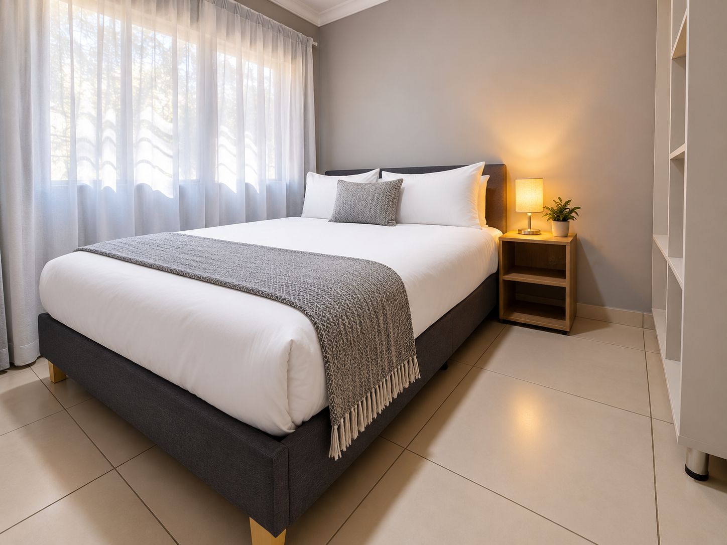 A modern bedroom with a large bed, a bedside table with a lamp, and a view of trees through the window.