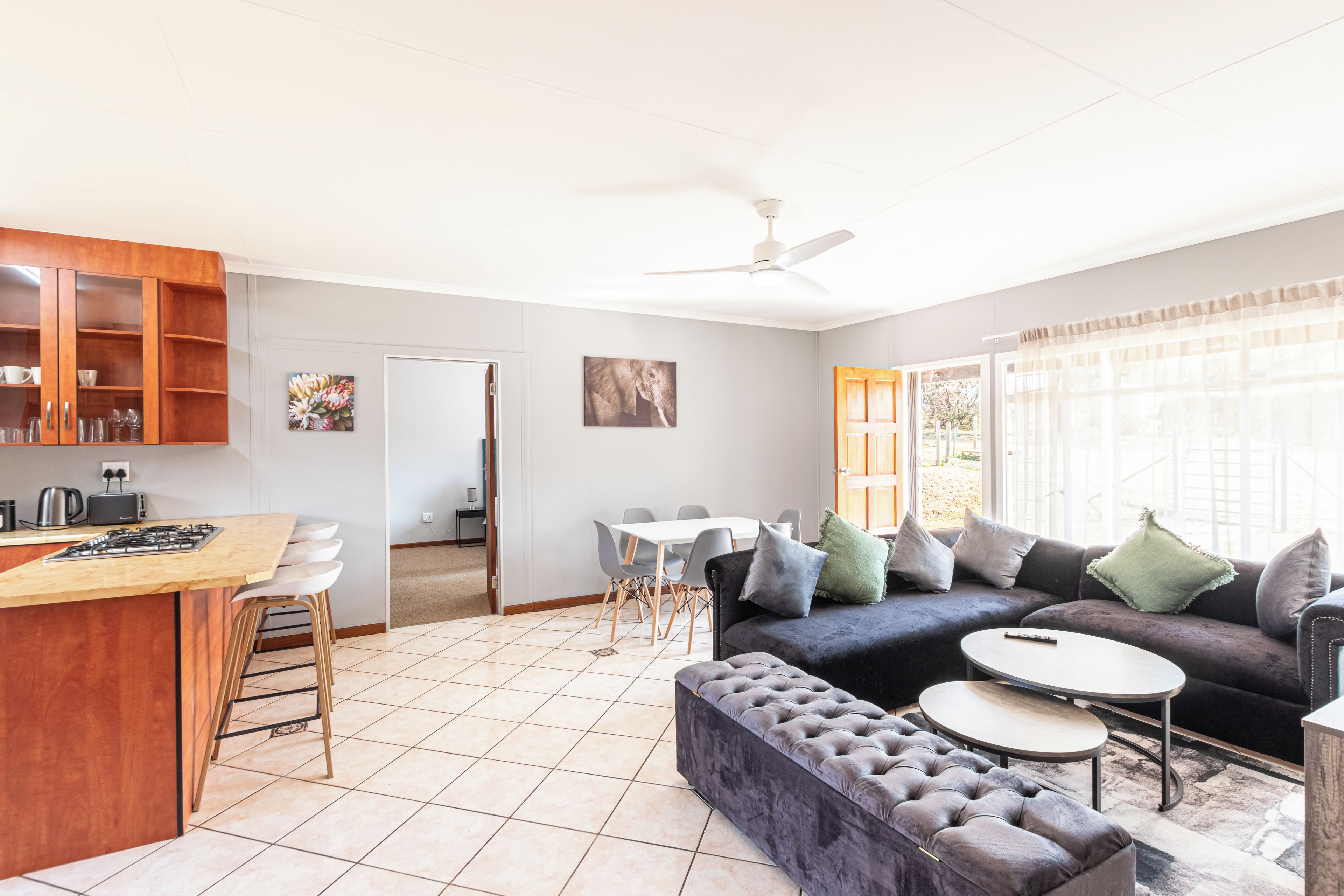 A modern kitchen with a bar area, a dining set, a sofa, and a large window with curtains.