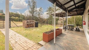 A covered patio area with a brick barbecue, outdoor seating, and a fire extinguisher. - Forest View Self Catering (Krugersdorp)