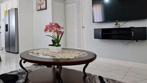 Una sala de estar moderna con una mesa redonda de cristal, un televisor de pantalla plana montado en la pared y una orquídea en maceta sobre la mesa.